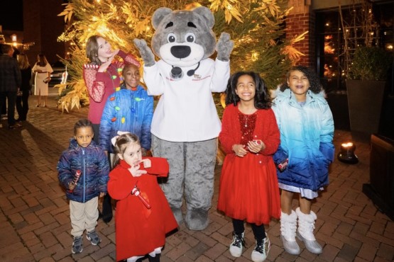Several girls smile as they pose with Dr. Bear in front of a festively lit holiday tree.