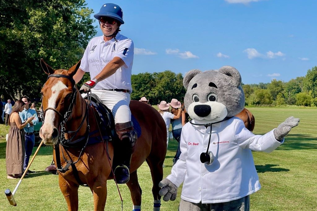 Children's National Hospital mascot, Dr. Bear, standing next to a polo player seated on their horse.